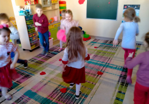 Dzieci biegają wokół serduszek rozłożonych na dywanie.